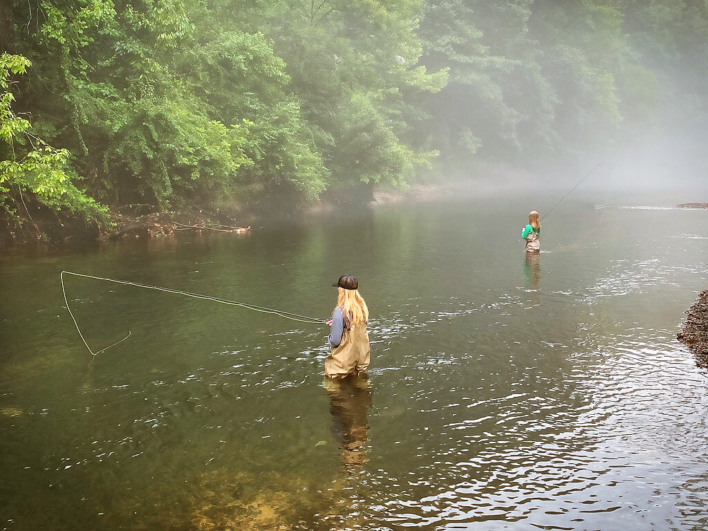 Two anglers wading in a misty river on a family outing