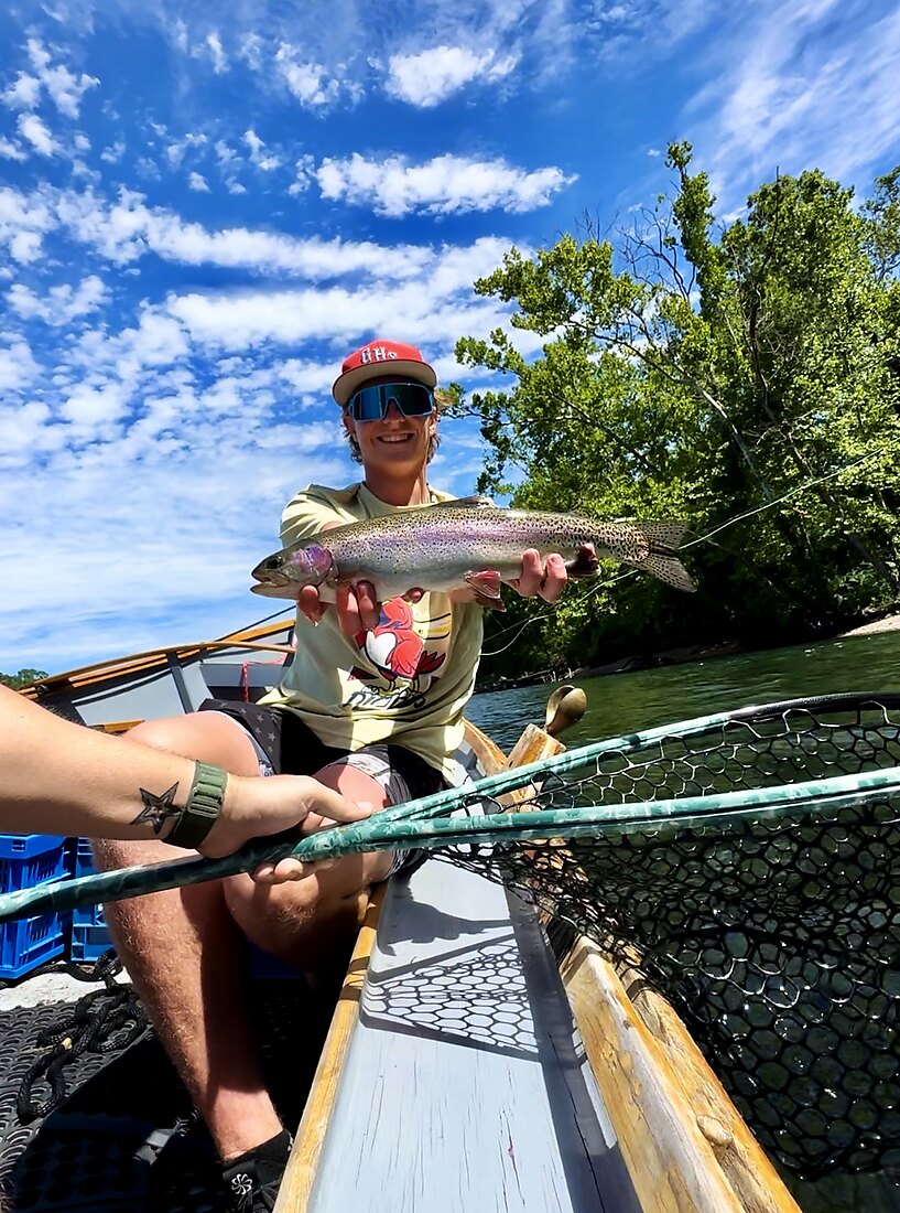 Smiling client holding a rainbow trout from a drift boat
